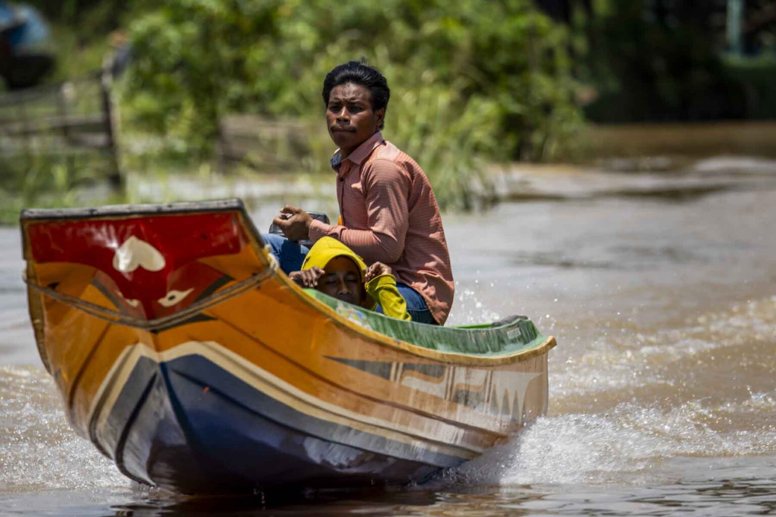 A young man drives a yellow and blue boat on Tonle Sap Lake near Siem Reap in Cambodia.