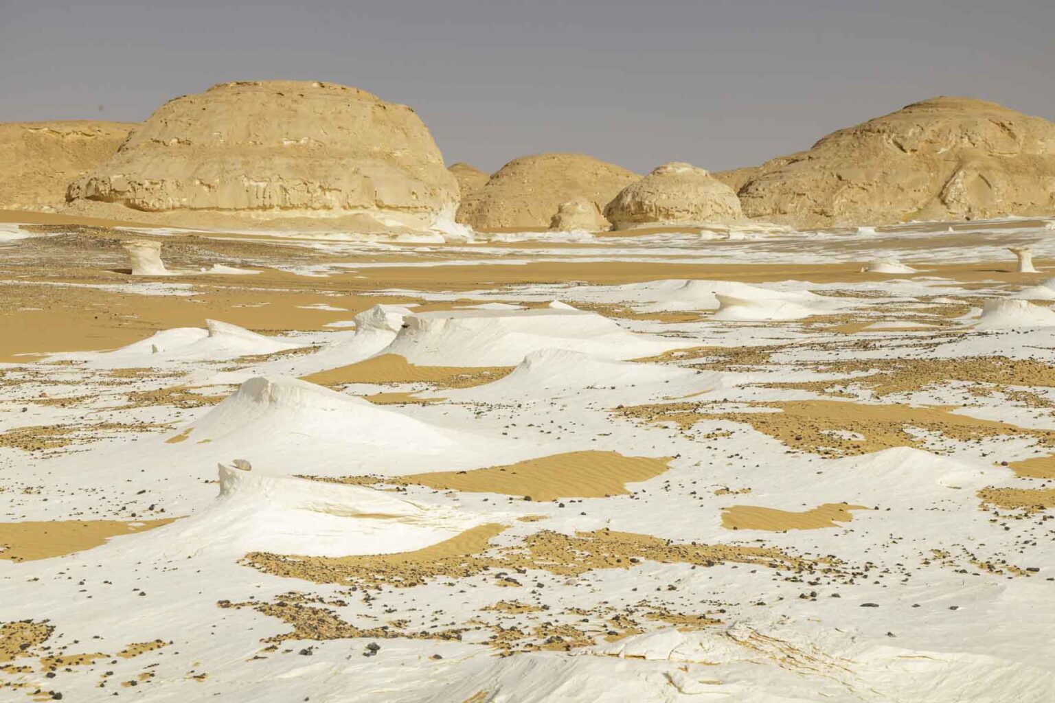 Piles of pure white sand in the desert with mounds of hard sand in the background.