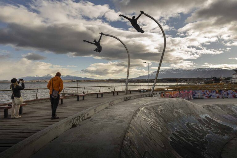 A man walks alongside a lake under two sculptures of people flying